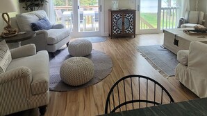 Un salon spacieux avec un plafond haut, un ventilateur de plafond, un grand téléviseur à écran plat et une vue sur un lac, visible à travers les portes-fenêtres coulissantes.