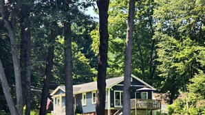 Une maison dotée d’une terrasse, entourée d’arbres et bordée par un plan d’eau.