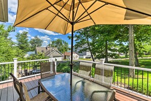A glass-top table with a beige umbrella, surrounded by wicker chairs, on a wooden deck with a white railing. - Walk to Lake: Middlefield Home w/ Fire Pit (Middlefield)