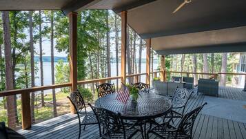 Une terrasse extérieure couverte, dotée d’une table ronde et de chaises, qui offre une vue sur un lac et est entourée d’arbres.
