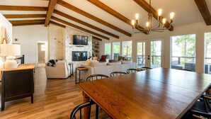 Un vaste espace de vie comprenant une grande table à manger en bois, une cheminée en pierre et un plafond haut avec des poutres apparentes.