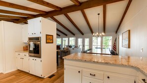 Une cuisine spacieuse avec des meubles blancs, un plan de travail en granit et un plafond en bois.
