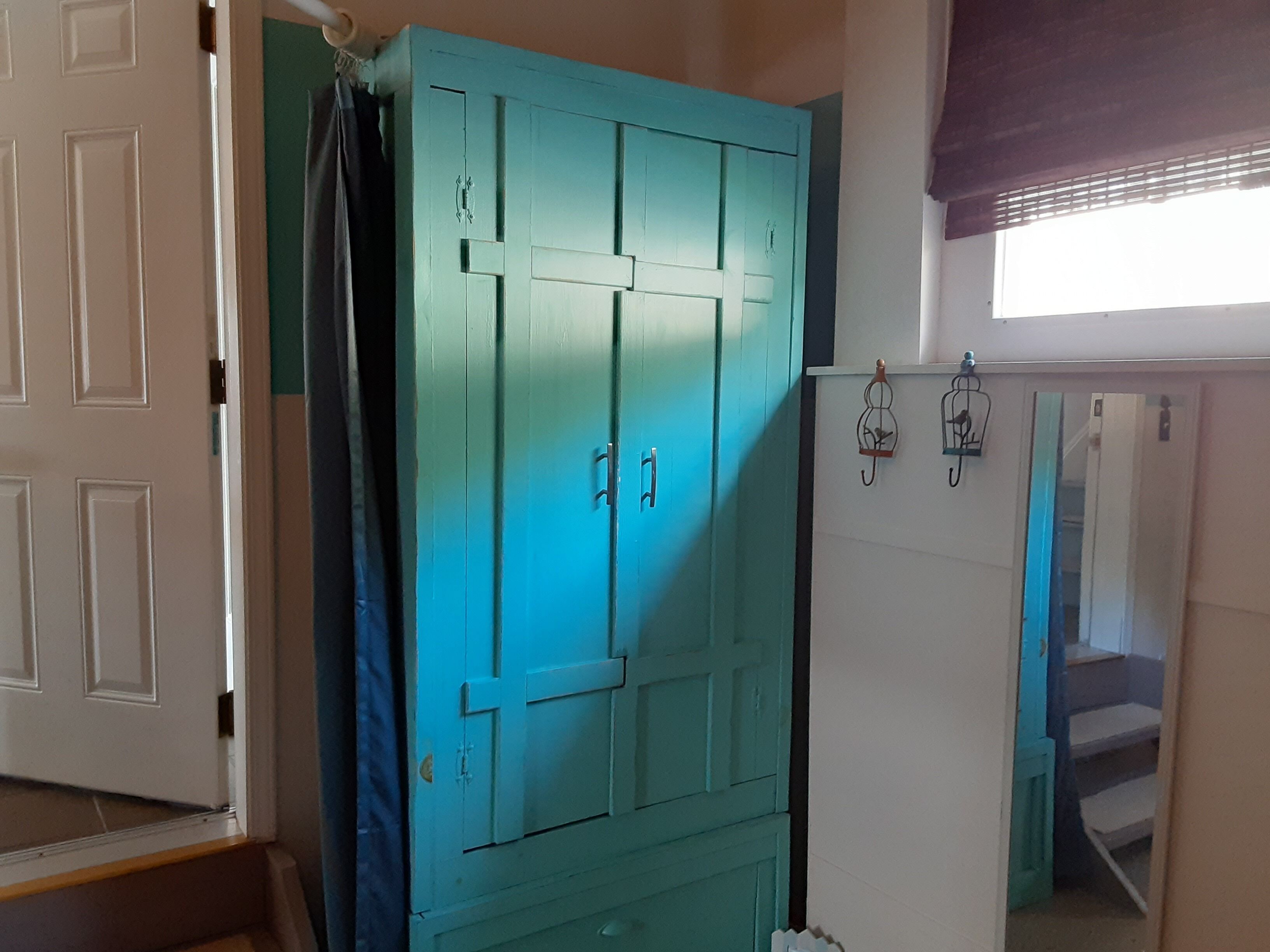 A room with a teal wardrobe, a white door, and a window with blinds.