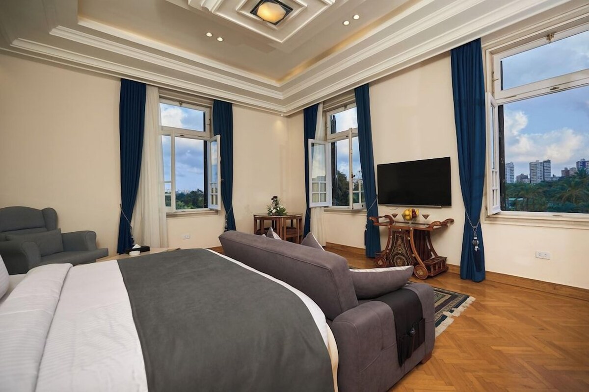 Een hotelkamer met een groot bed, een bank, een televisie en uitzicht over de stad.