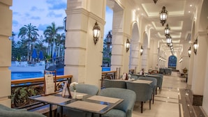 Un restaurant doté d’une terrasse avec vue sur une piscine, présentant un intérieur moderne avec des chaises et des tables bleues, ainsi que des appliques murales décoratives.