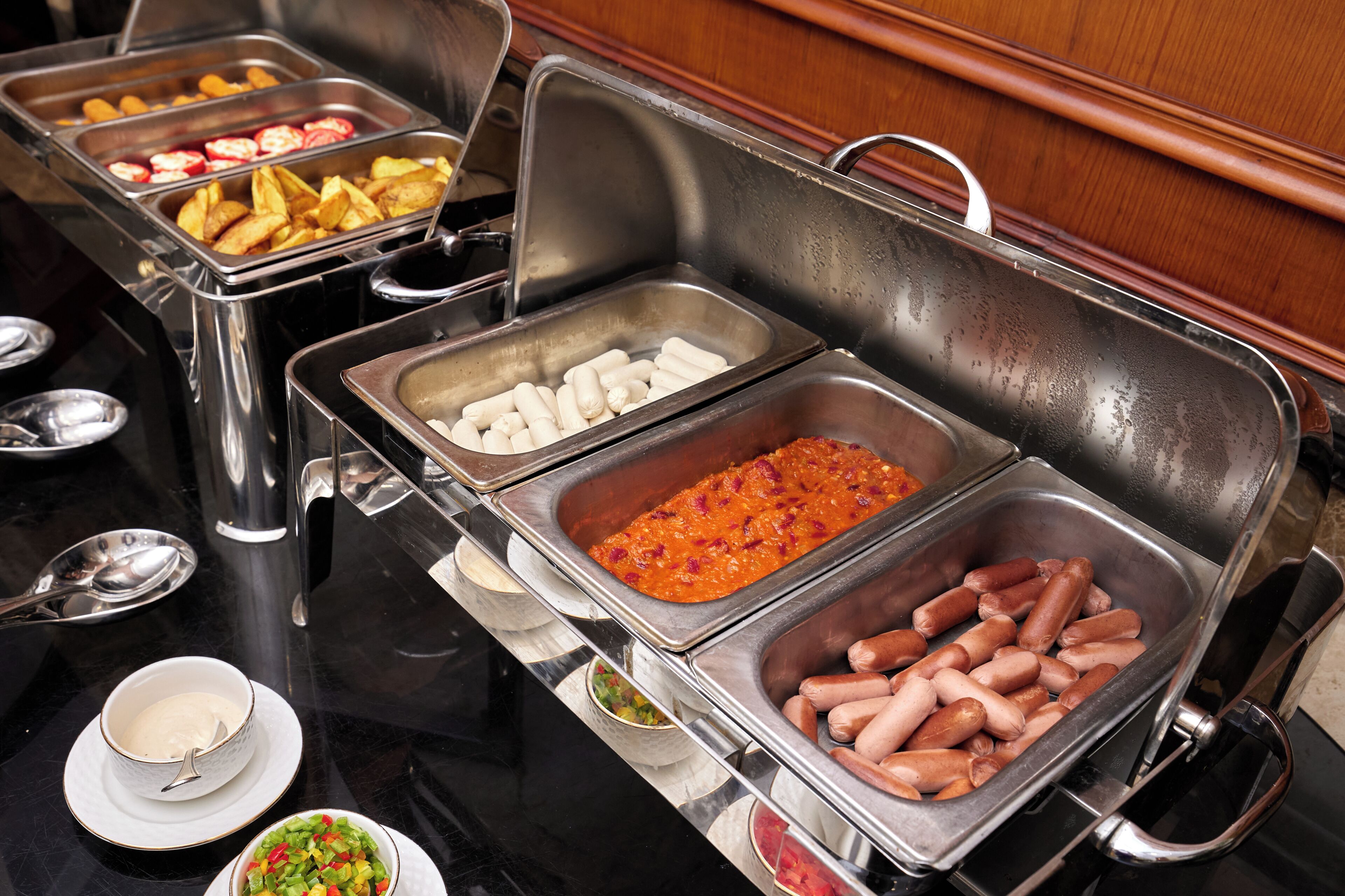 A buffet with various food options including sausages, potatoes, and other dishes.
