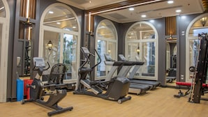 Une salle de sport équipée de divers appareils d’exercice, dotée de grandes fenêtres et d’un plancher en bois.