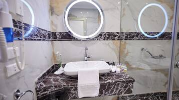 Un baño con lavamanos de mármol, dos espejos redondos, una toalla y una ducha.