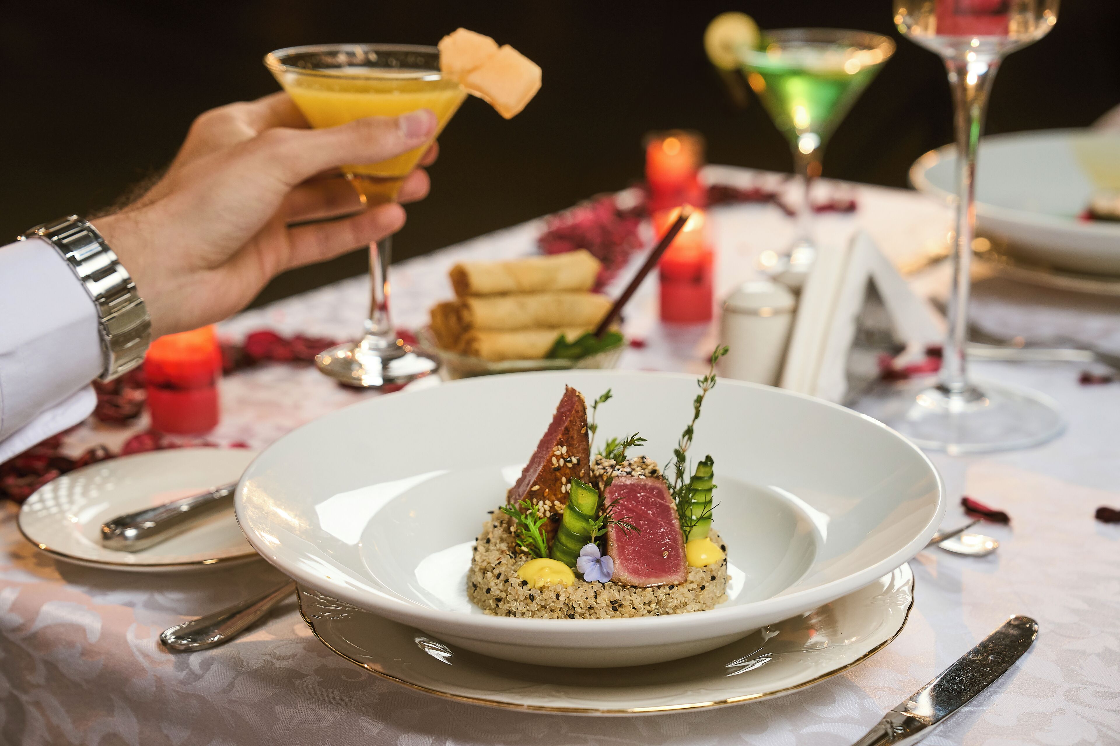 Una mesa de comedor con un plato de comida, un vaso de bebida y una vela.
