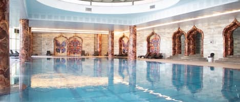 Una piscina interior con techo de vidrio, columnas de mármol y decoraciones murales ornamentadas.