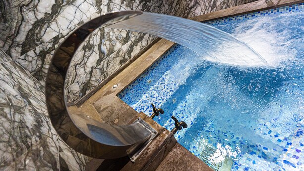 Una piscina in marmo con un elemento d'acqua curvo e due rubinetti.