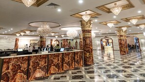Un'ampia hall con pavimento in marmo, soffitti decorati con cornici dorate e numerosi lampadari.