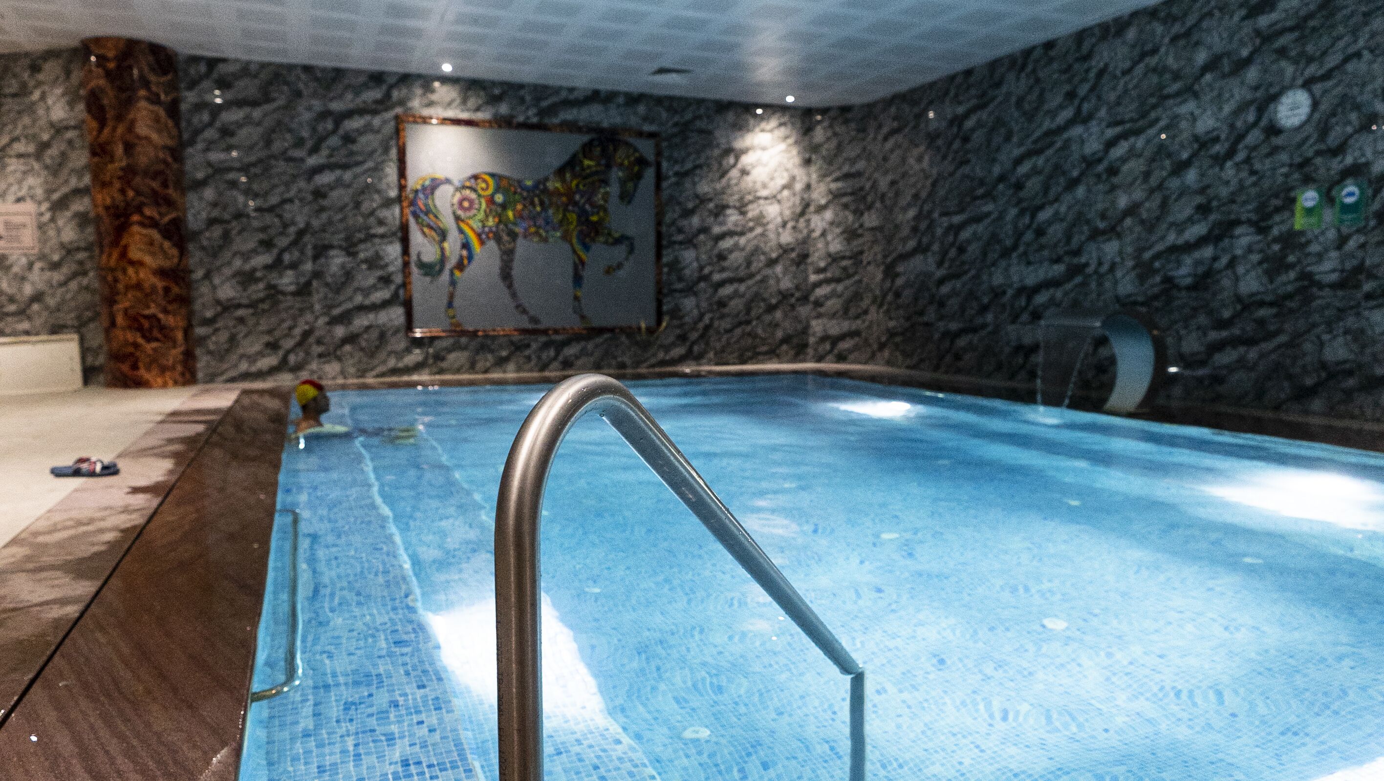 An indoor swimming pool with a marble wall and a colorful mural.