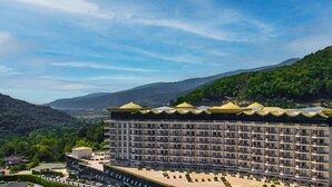 Hotel moderno a più piani con balconi su ogni livello, immerso nel verde e con montagne sullo sfondo.