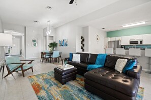 A modern living room with a dark leather sofa, a coffee table, and a dining area with a table and chairs. - Last Minute Disney Getaway! Villa with Private Pool & Hot Tub. Book Now! #44 (Orlando)