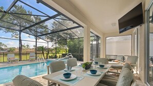 Un espace extérieur abrité comprenant une piscine, des sièges et une table dressée pour les repas.