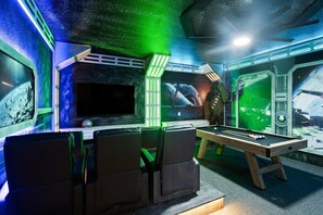 A room with a pool table, a flat-screen TV, and a large window with a space-themed mural.
