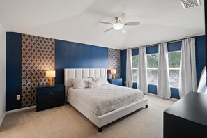 A bedroom with a bed, nightstands, a ceiling fan, and a window with curtains.