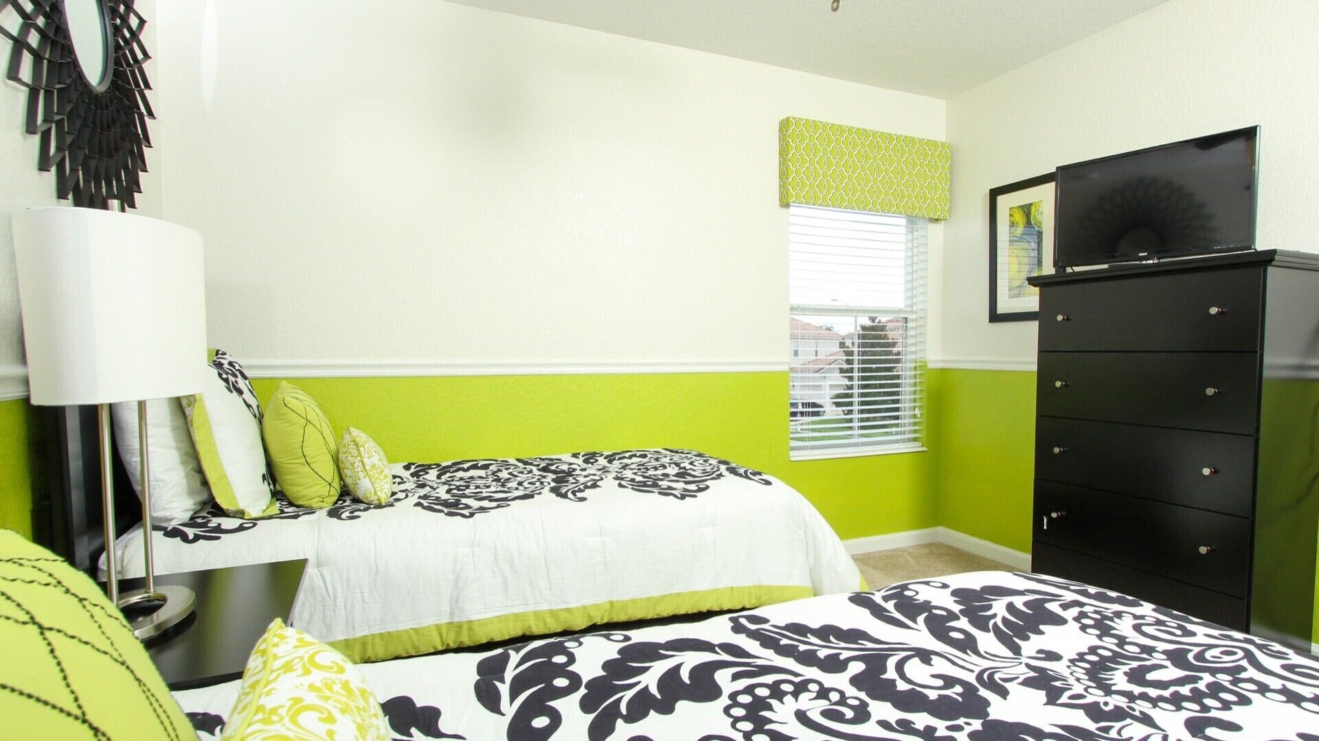 A bedroom with a bed, a dresser, a lamp, and a window with blinds.