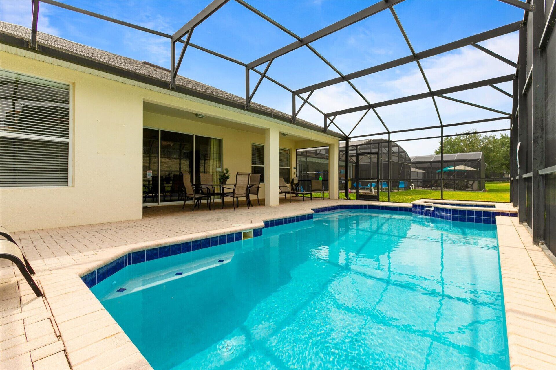 A swimming pool with a glass enclosure, patio chairs, and a covered outdoor area.