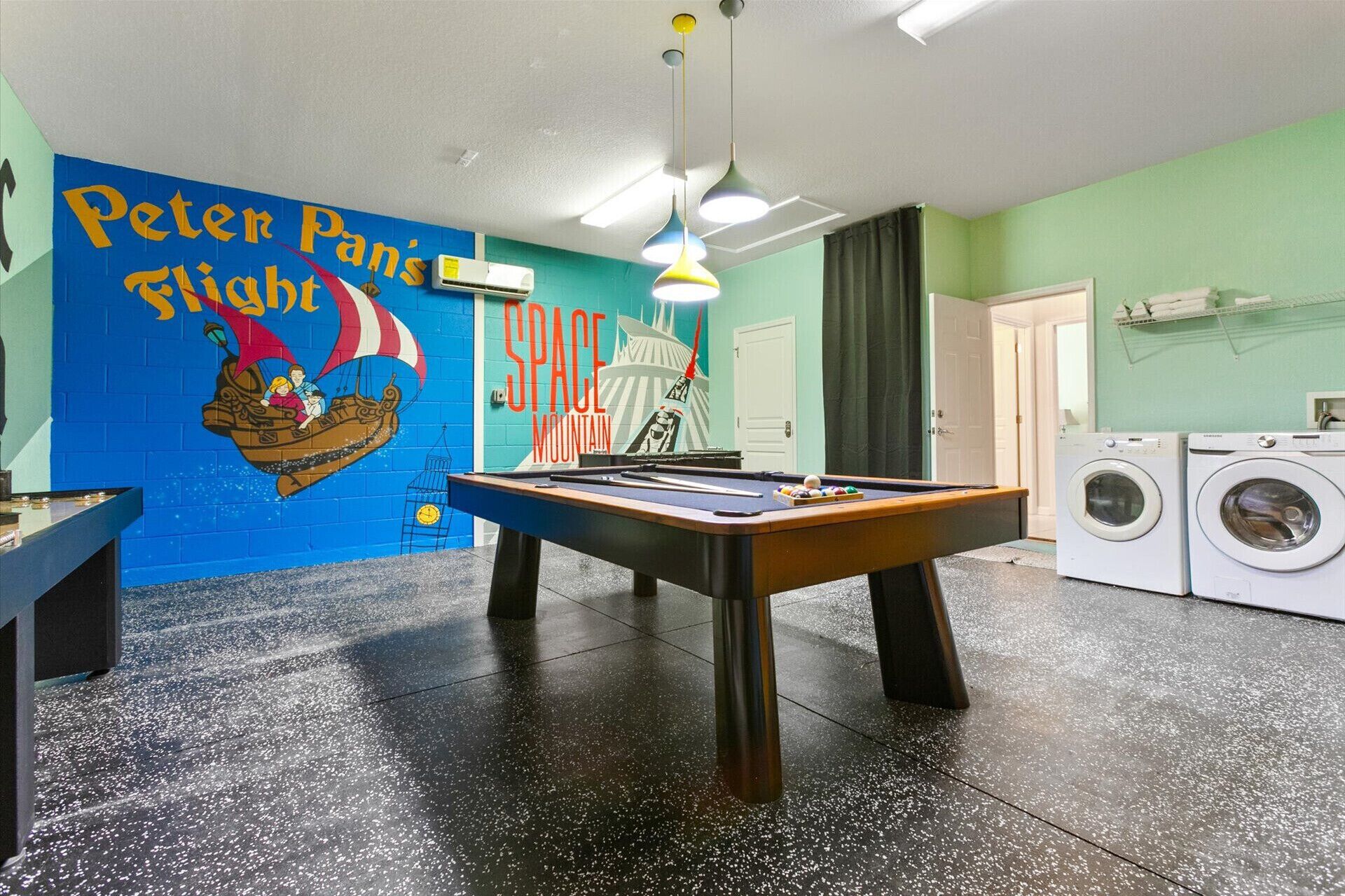 A room with a pool table, a mural, a washing machine, and a door.