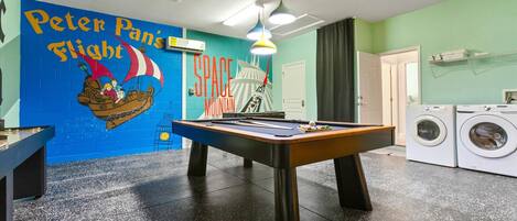 A room with a pool table, a mural, a washing machine, and a door.
