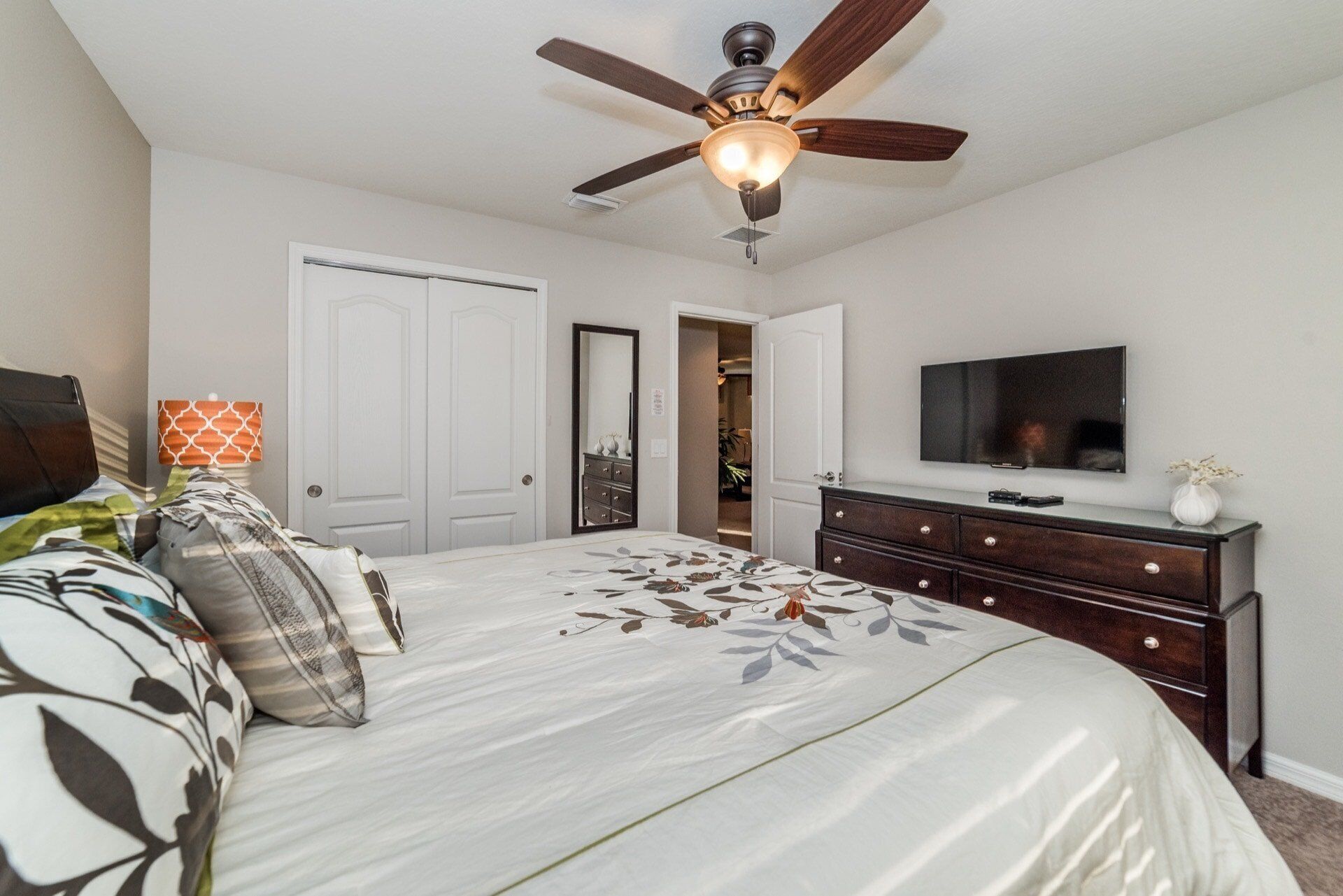 A bedroom with a bed, a ceiling fan, a dresser, a TV, and a door leading to a closet.