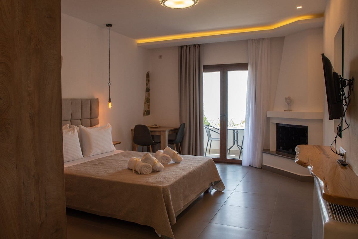 A hotel room with a bed, a desk, a chair, a fireplace, and a balcony with curtains.