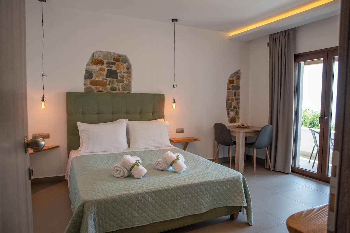 A neatly made bed with a green quilt, two bedside tables with lamps, a stone accent wall, and a balcony with a table and chair.