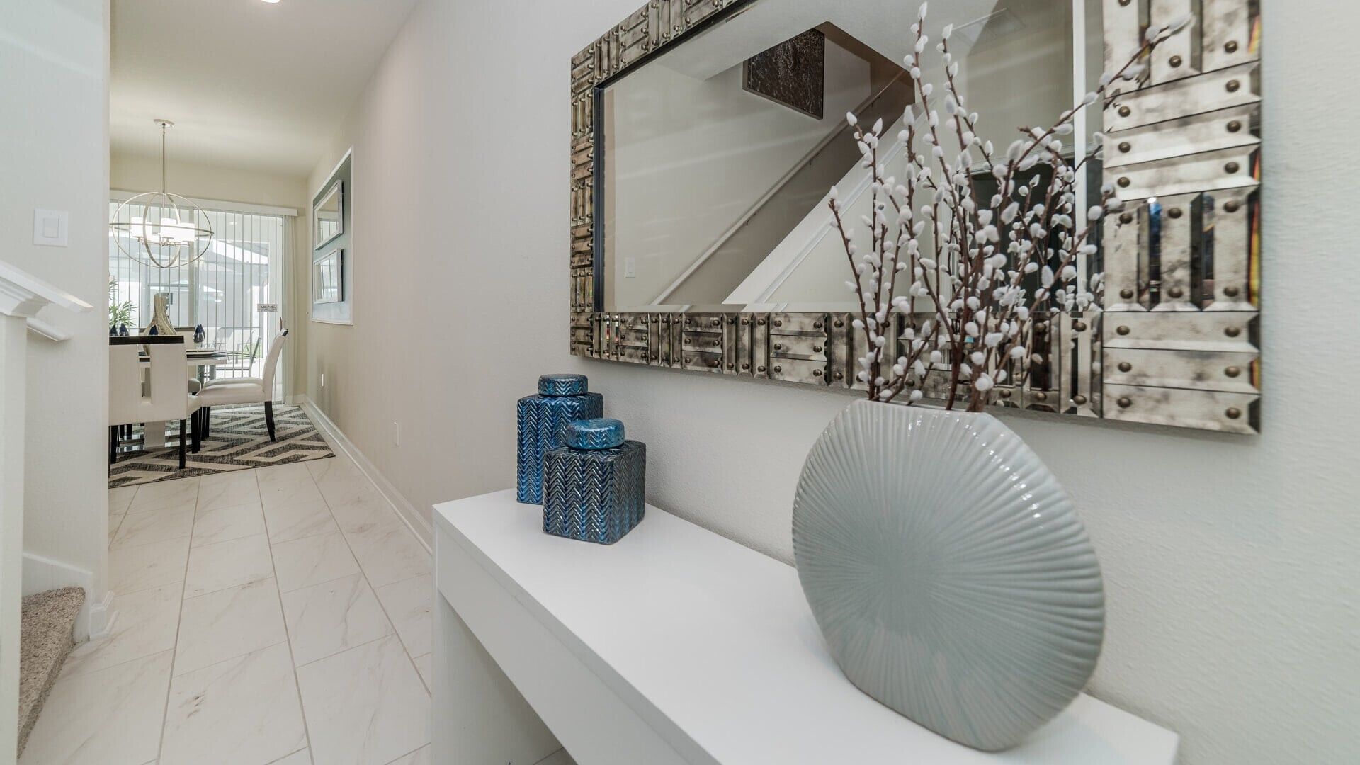 A hallway with a white console table, decorative vases, and a mirror with a metal frame.