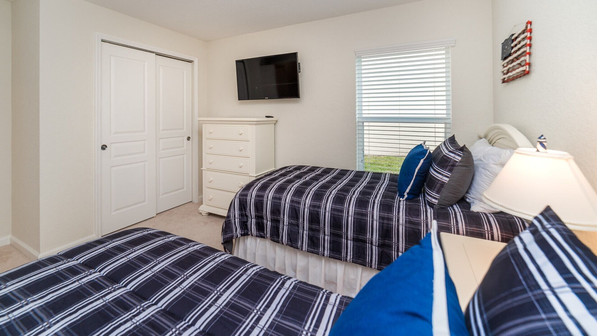 A bedroom with two beds, a dresser, a TV, and a window with blinds.