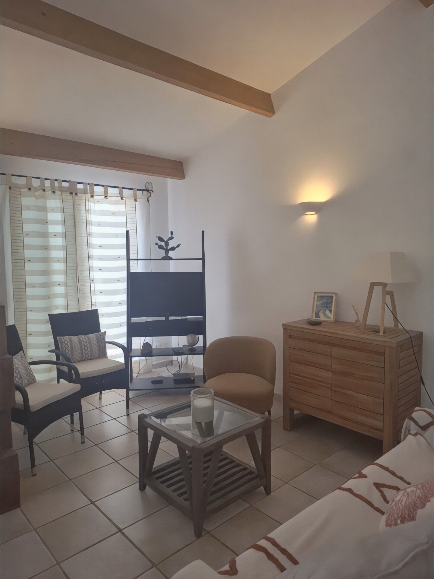 Ein Wohnzimmer mit einer Couch, Sesseln, einem Couchtisch, einem Fernseher, einer Holzkommode und einem Fenster mit Vorhängen.