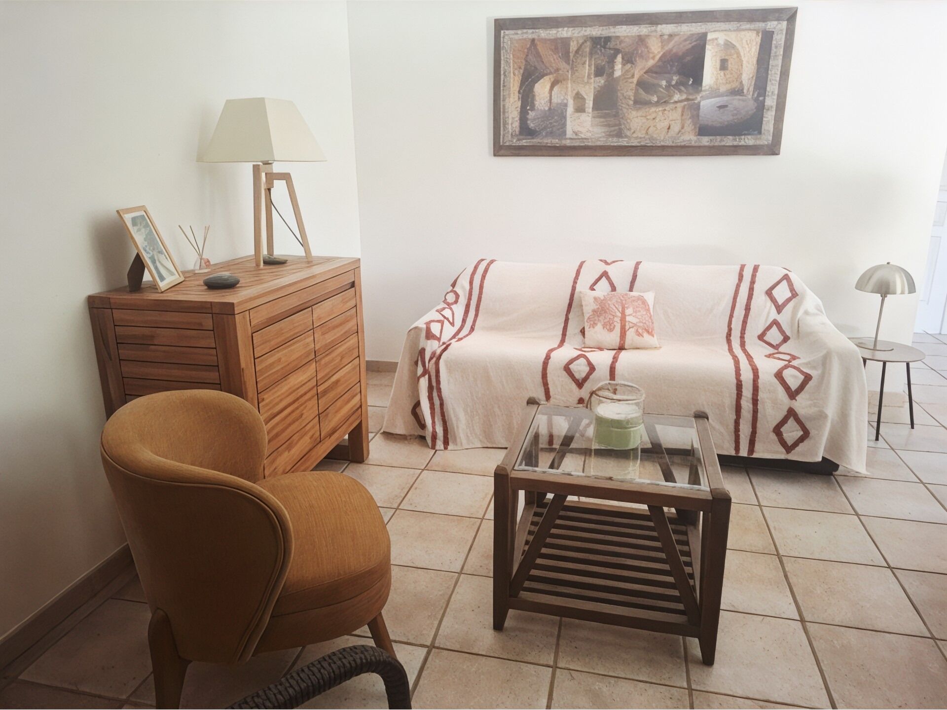 Una sala de estar con un sofá, un aparador de madera, una silla, una mesa de centro de vidrio y una lámpara.