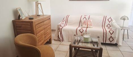 Una sala de estar con un sofá, un aparador de madera, una silla, una mesa de centro de vidrio y una lámpara.