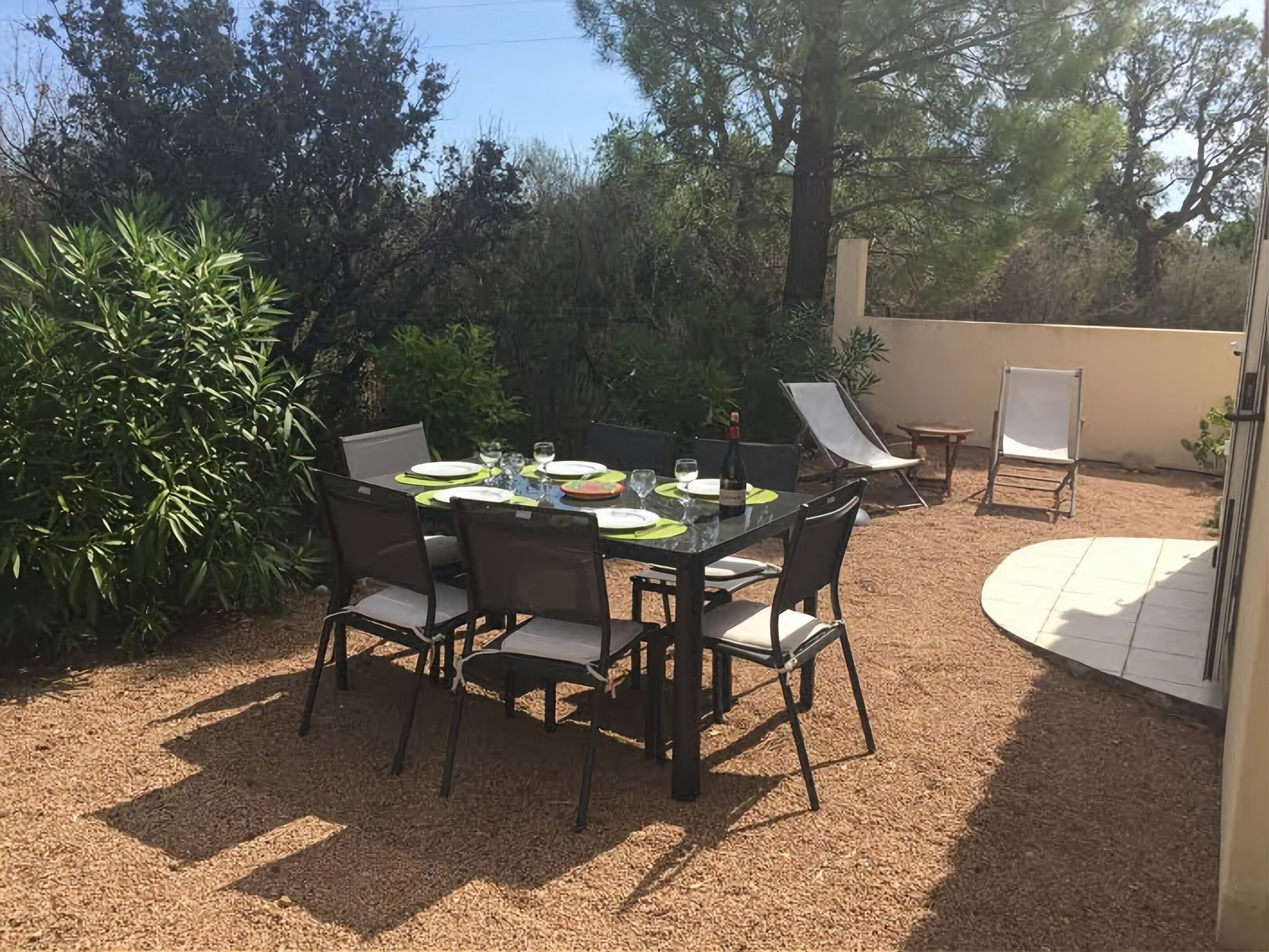 Patio esterno con tavolo apparecchiato per mangiare, circondato da sedie e una piccola zona relax con una sedia e un tavolino.
