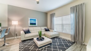 A living room with a sofa, a coffee table, a lamp, a painting, and a window with curtains. - Last Minute Disney Getaway! Townhouse with Private Pool. Book Now! #20876 (Orlando)