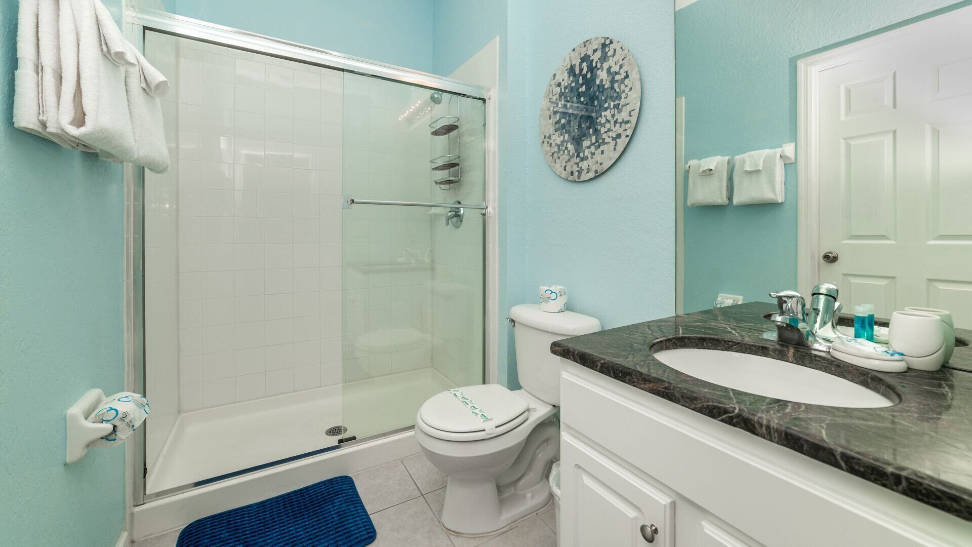 A bathroom with a glass-enclosed shower, a toilet, a sink with a marble countertop, and a wall-mounted mirror.