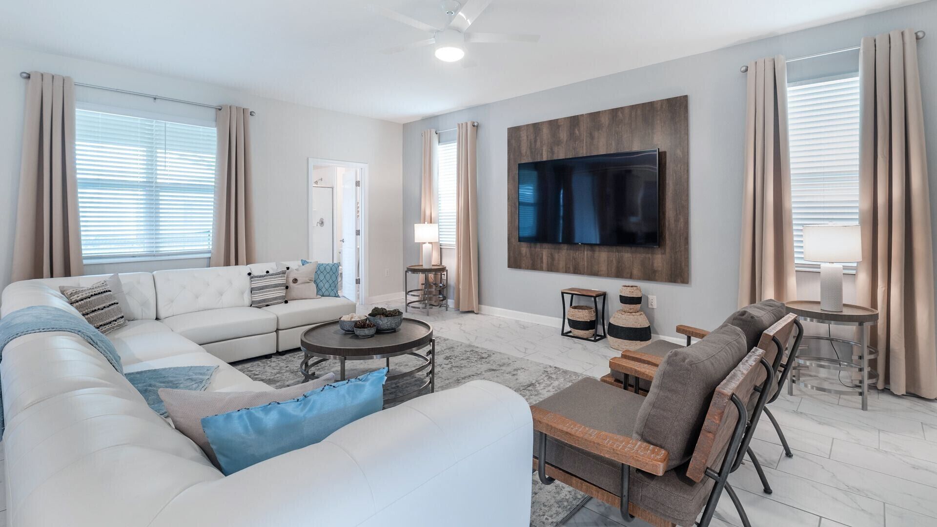 Ein modernes Wohnzimmer mit einer Couch, Sesseln, einem Couchtisch und einem an der Wand befestigten Fernseher.