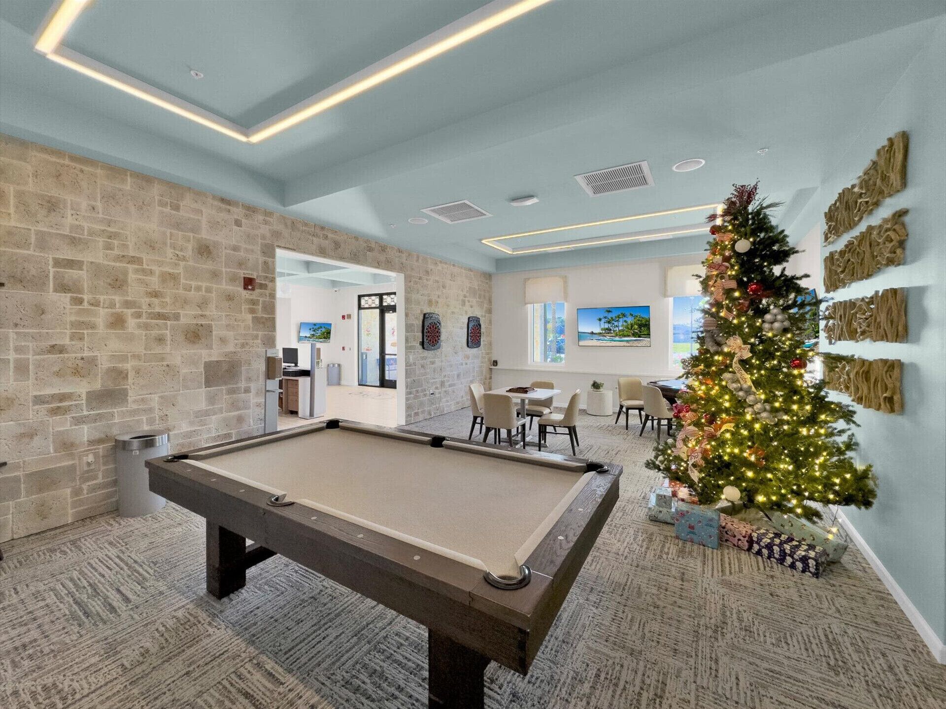A pool table in a room with a brick wall, a Christmas tree, and a dartboard.