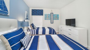 Cozy bedroom with striped bedding, a flat-screen TV, and a bedside table with a lamp.