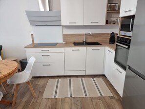 A modern kitchen with white cabinets, a stainless steel refrigerator, a built-in oven, and a wooden countertop.
