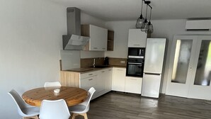 Une cuisine moderne avec des meubles blancs, une table à manger en bois et un four encastré.