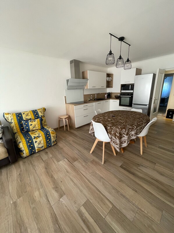 A compact kitchen with modern appliances, a dining area with a patterned tablecloth, and a sofa with a floral design.
