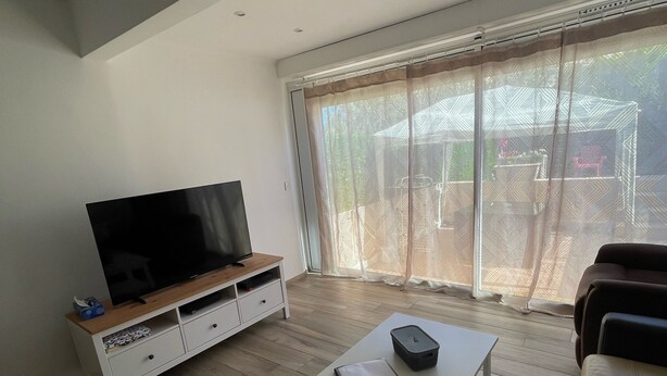 Un salon moderne avec un téléviseur à écran plat posé sur un meuble télé en bois, une table basse blanche avec une télécommande et un canapé en cuir.