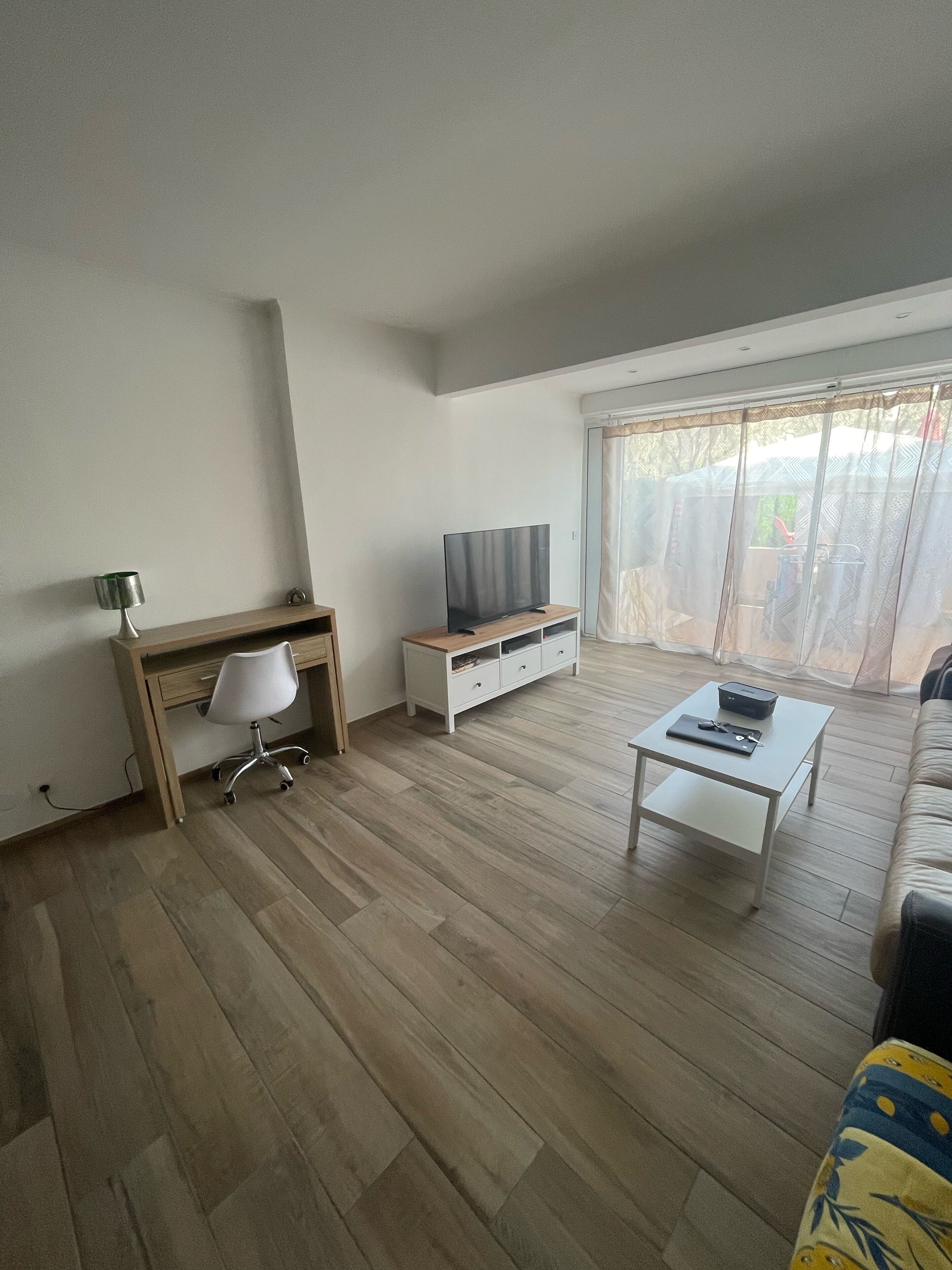 Een moderne woonkamer met een houten bureau, een witte bureaustoel, een televisie op een witte standaard, een salontafel en een bank.