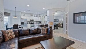 A modern living room with a leather sofa, a dining area, and a kitchen with white cabinets and a built-in oven. - Last Minute Disney! Private Pool, Hot Tub, Game Room & Themed Bedrooms. Book Now! #54401 (Orlando)