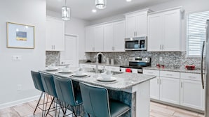 Una cocina moderna con armarios blancos, encimeras de granito y una isla central con taburetes de bar.