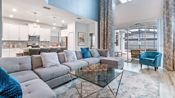 Un salón amplio con un sofá gris, una mesa de centro de cristal y un sillón azul.