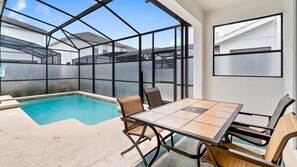 Un espace piscine doté d’un patio fermé par des baies vitrées, d’une table et de chaises.