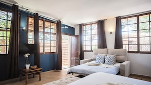 Een slaapkamer met een bed, een bank, een klein tafeltje met een plant en een raam met gordijnen.